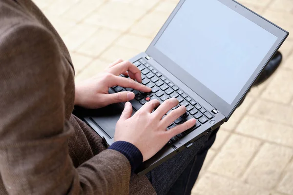 A Japanese man in a jacket operating a computer outdoors.