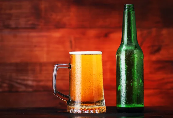Caneca cheia de cerveja com espuma e garrafa vazia — Fotografia de Stock
