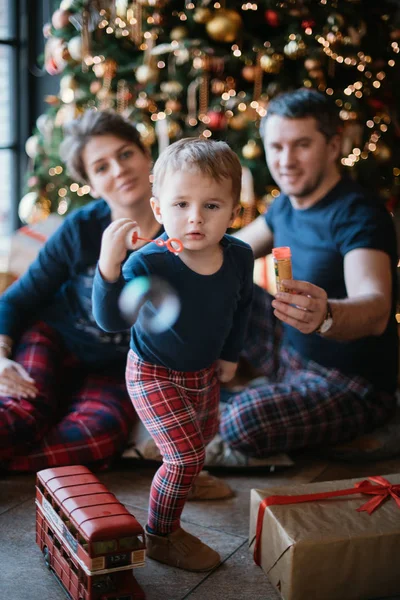 Family New Year. A family with a little boy is sitting under the Christmas tree.