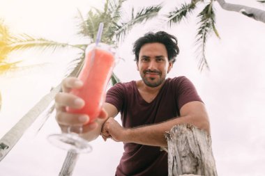 Yakışıklı bir adam elinde meyve kokteyli tutuyor ve gülümsüyor.