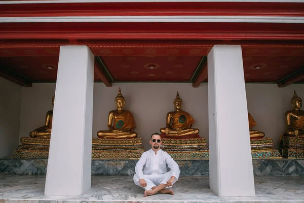 A man sits in a lotus position in a Buddhist palace on the backg