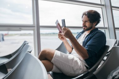 Havaalanının kapısında elinde telefon olan bir adam oturuyor..