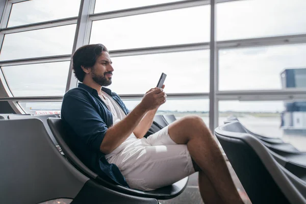 A man sits in a waiting room near the gate at the airport with a telephone. — Stock Photo, Image