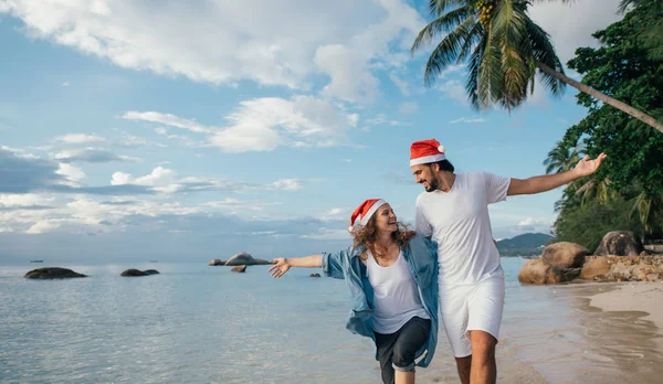 A young couple joyfully run along the sea in New Year's hats. — Stock Photo, Image