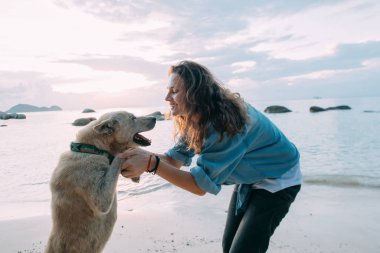 Kız gün batımında sahilde köpekle oynarken eğleniyor..