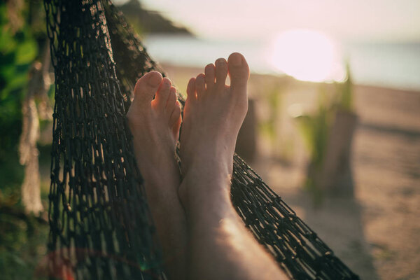 A man is resting in a hammock. Close-up of legs. Sunset light. Tropical island