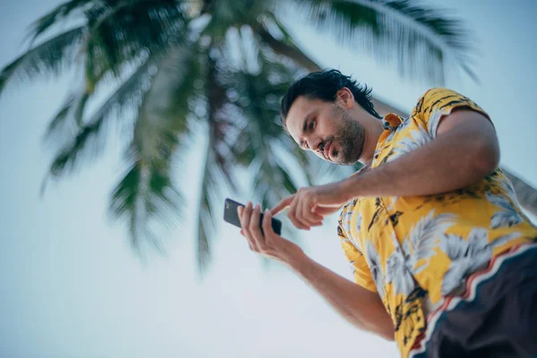A contented man is standing with a phone in his hands on a background of palm trees — Stock Photo, Image