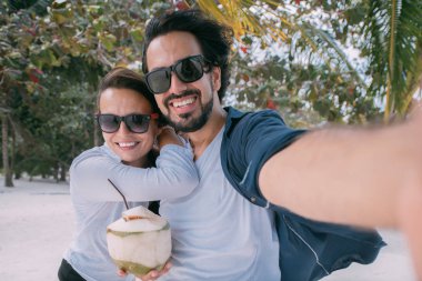 A pair of lovers take a selfie under a palm tree on a tropical b