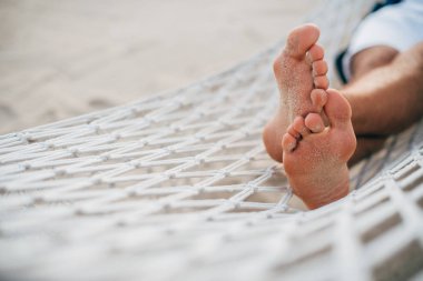 Bir adam hamakta dinleniyor. Bacakları yakın çekim. Gün batımı ışığı. Tropik ada