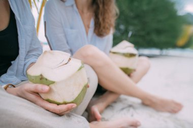 Yeşillik ve denizin arka planında taze hindistan cevizi olan ellerin yakın çekimi.