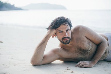 Yakışıklı bir adam okyanusun kıyısında kumların üzerinde yatıyor.. 
