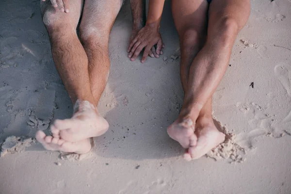 Dois homens gays estão sentados na areia junto ao oceano, de mãos dadas . — Fotografia de Stock