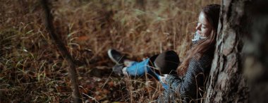 Bir kız yalnız güneşli bir günde bir ormana bir ağacın altında oturuyor.