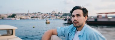 Deniz, şehir, iskele ve gemilerin arka planında genç bir adamın portresi