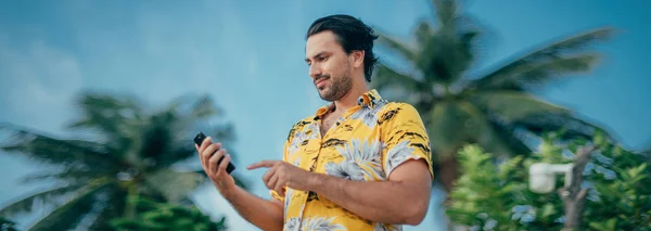 A contented man is standing with a phone in his hands on a background of palm trees
