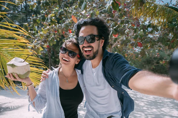 Een paar minnaars nemen een selfie onder een palmboom op een tropisch strand — Stockfoto