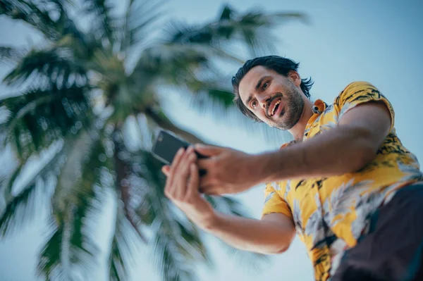 A contented man is standing with a phone in his hands on a background of palm trees