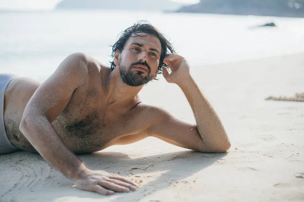 海のそばの砂の上にハンサムな男が横たわっている. — ストック写真