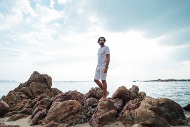 Tropikal sahilde bir adam Deniz kenarındaki taşlarda.