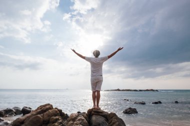 Tropikal sahilde bir adam Deniz kenarındaki taşlarda.