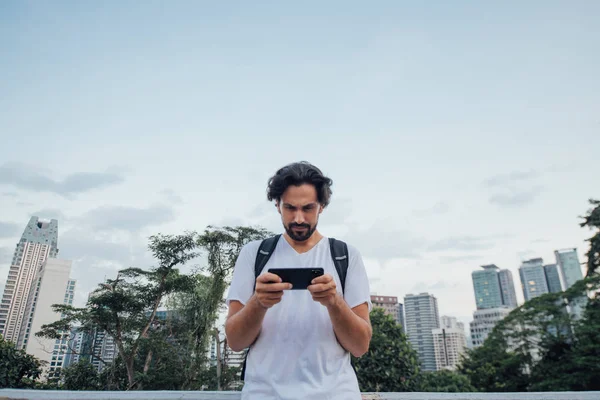 Een man zoekt een route aan de telefoon tegen de achtergrond van een metropool. — Stockfoto