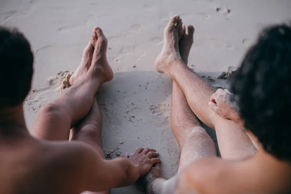 Dos hombres gay están sentados en la arena junto al océano, tomados de la mano . — Foto de Stock