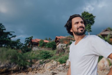 Tayland ulusal evlerinin arka planında sahilde bir erkek turistin portresi