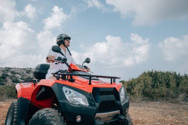 A man sits on a quad in a helmet and glasses in the mountains