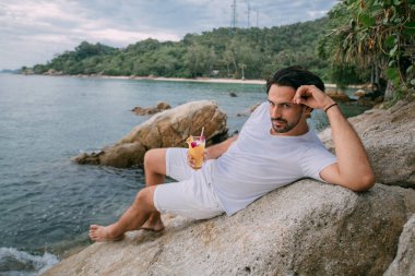 Bir adam okyanusun kıyısındaki bir taşın üzerinde oturuyor.