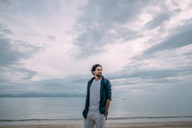 Yalnız bir adam bulutlu bir günde sahilde yürüyor.