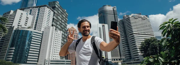 Um homem tira uma selfie contra o pano de fundo dos arranha-céus — Fotografia de Stock
