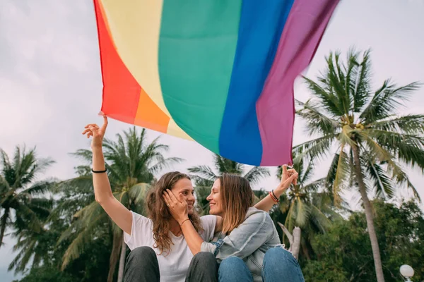 Dwie kobiety z tęczową flagą na plaży na tle palmy — Zdjęcie stockowe