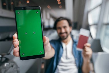 Havaalanının kapısındaki bekleme odasında elinde telefon olan bir adam oturuyor. Ön planda krom ekran olan yakın plan bir telefon. Genç bir gezgin kamerada yeşil ekranlı bir telefon gösteriyor..
