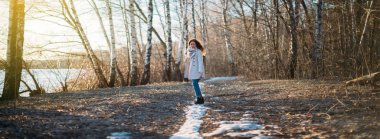 Bir kız son karda bir orman izi boyunca yürür. Hafif bir yağmurluk içinde genç bir kadın mutlu yürüyüşler, gün batımında ağaçlar arasında yol boyunca atlama