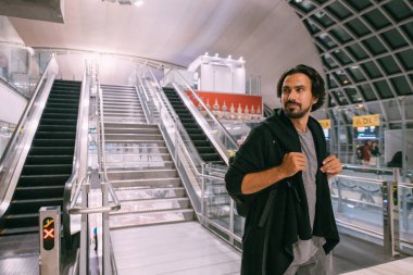 Havaalanındaki yürüyen merdivenin yanında bir adam var. Sırt çantalı genç bir adam terminalden uçağa biniyor.