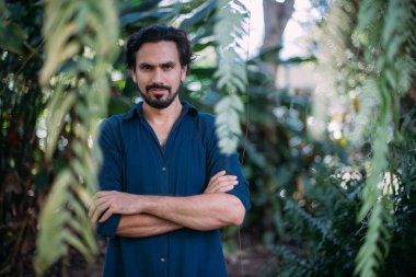 Yeşil yapraklı bir adamın kavramsal portresi. Güzel esmer adam, tropik çalıların arasında poz veren bir model. Yakın plan.