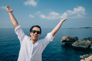 Denize bakan kayalıklarda bir adam. Beyaz elbiseli yakışıklı adam kayalık sahildeki okyanus manzarasının tadını çıkarıyor. # Denizin ötesindeki genç adam #