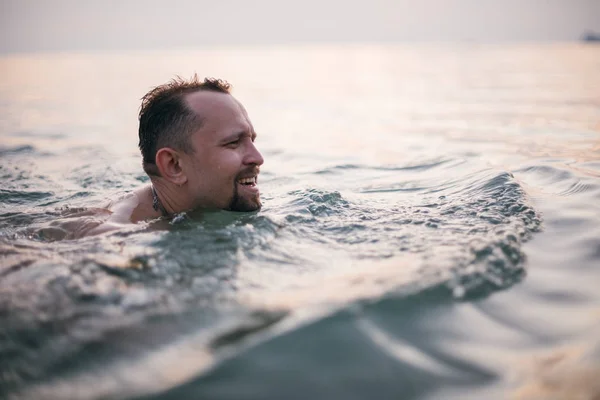 A man swims in the ocean at sunset. A young guy swims in calm water in the sea on a tropical island. Holidays in the tropics