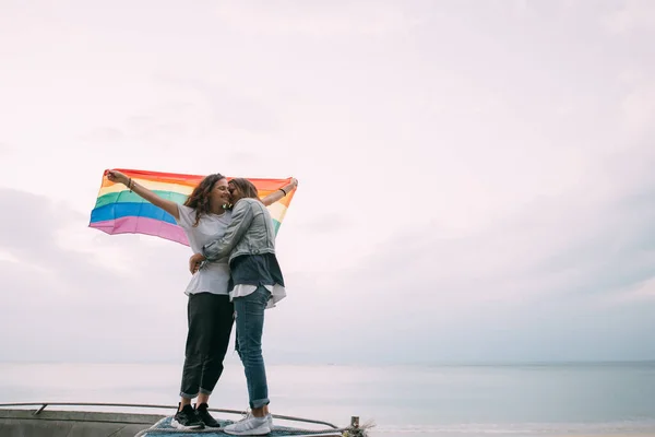 Dwie Kobiety Tęczową Flagą Plaży Pod Niebem Dwie Młode Lesbijki — Zdjęcie stockowe