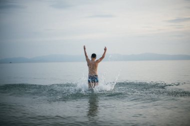 Bir erkek gün batımında akşam ve okyanusun tadını çıkarır. Tropikal bir adada, okyanusun sakin sularında yüzen genç bir adam. Tropik bölgelerde tatiller