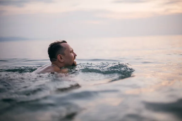 A man swims in the ocean at sunset. A young guy swims in calm water in the sea on a tropical island. Holidays in the tropics