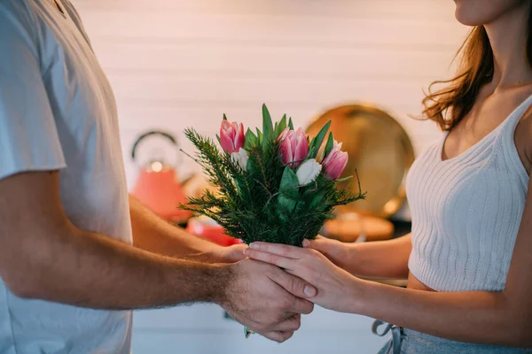 International Women\'s Day. Young couple in the morning in the kitchen at home. A man gives a woman a bouquet of tulips on March 8 in a beautiful stylish kitchen.