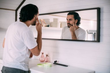 Yakışıklı bir adam aynaya bakar. Erkeklerin kişisel bakımı. Genç bir adam yatak odasındaki aynada kendini muayene ediyor..