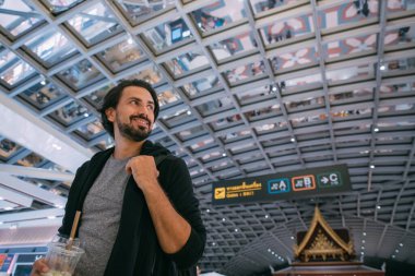 Havaalanında sırt çantalı genç bir adam. Neşeli adam terminalde yürüyor, uçağın uçmasını bekliyor.