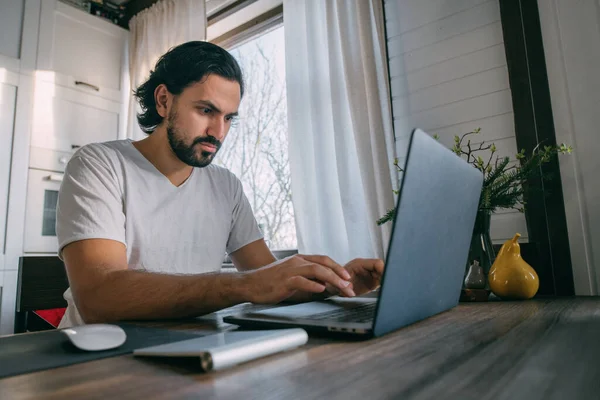 Workplace at home. A man works at a laptop at home, sits at a table in the living room during the day. Work from home.