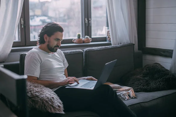 在家工作 一个男人在家里的笔记本电脑上工作 白天坐在客厅的沙发上 打电话 在家工作 — 图库照片