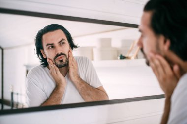 Yakışıklı bir adam aynaya bakar. Erkeklerin kişisel bakımı. Genç bir adam yatak odasındaki aynada kendini muayene ediyor..