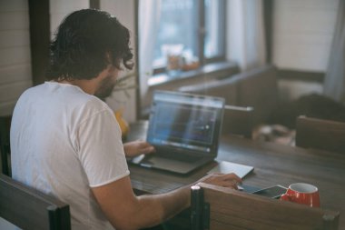Evdeki işyerinde. Evde dizüstü bilgisayarda çalışan bir adam gün boyunca oturma odasındaki bir masada oturuyor. Evden çalış..