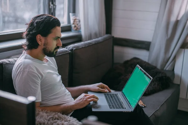 Workplace at home. A man works on a laptop at home, sits on a sofa in the living room during the day, talks on the phone. Work from home.