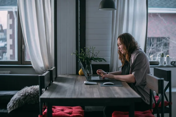 에서의 여성은 집에서 노트북으로 일하고 거실의 소파에 앉아서 전화로 이야기를 — 스톡 사진